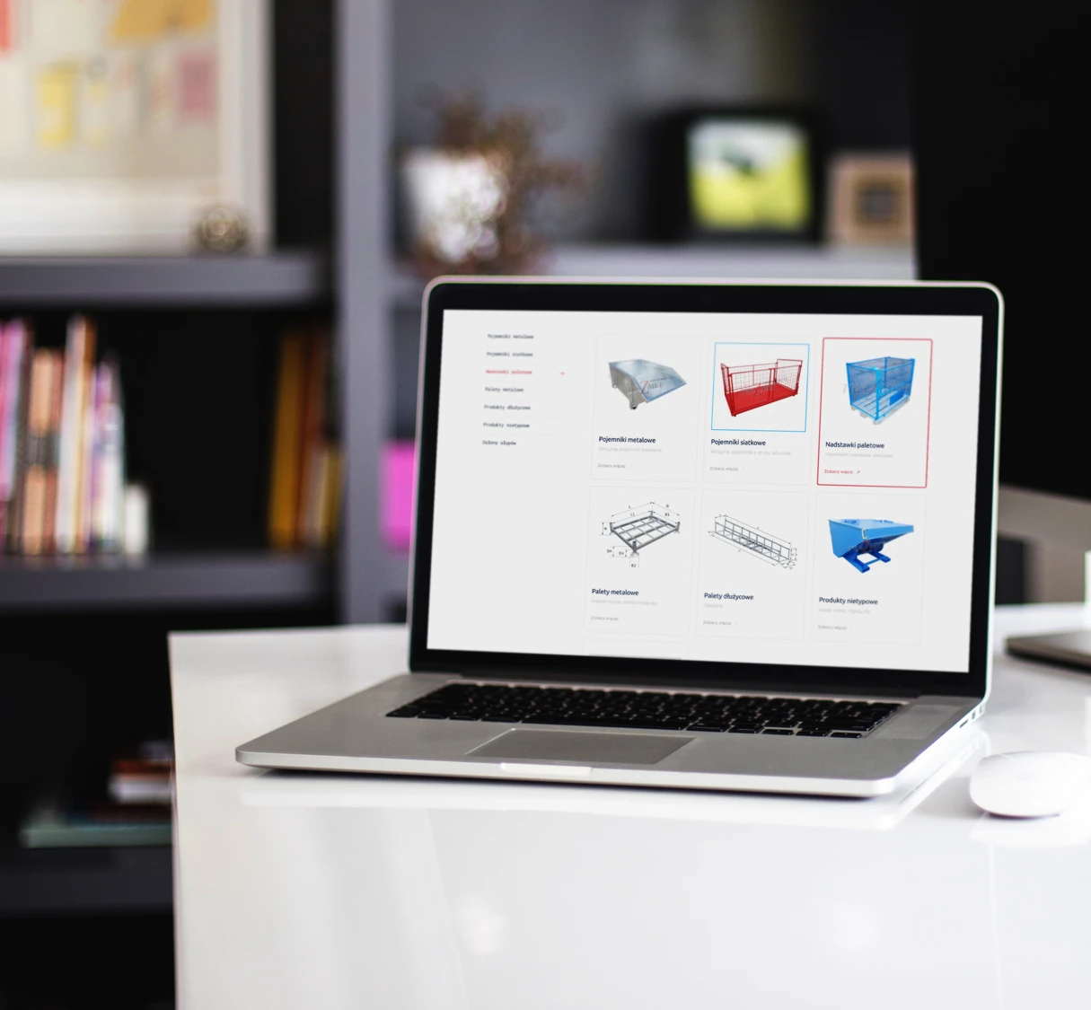 Obraz przedstawia laptop na biurku, na którego ekranie widoczny jest katalog produktowy z różnymi elementami konstrukcyjnymi, takimi jak pojemniki siatkowe, nadstawki i palety stalowe